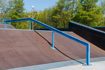 Fototapeta premium modern skate park, brown skateboard ramp with blue metal pipe outdoors in city park in summer for skateboarding, roller skating and bicycle riding, extreme sport