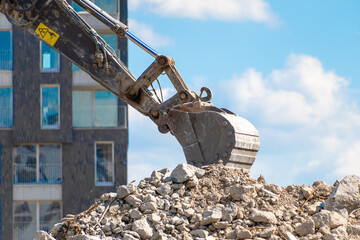 Obraz premium Excavator digging rubble near modern building under blue sky