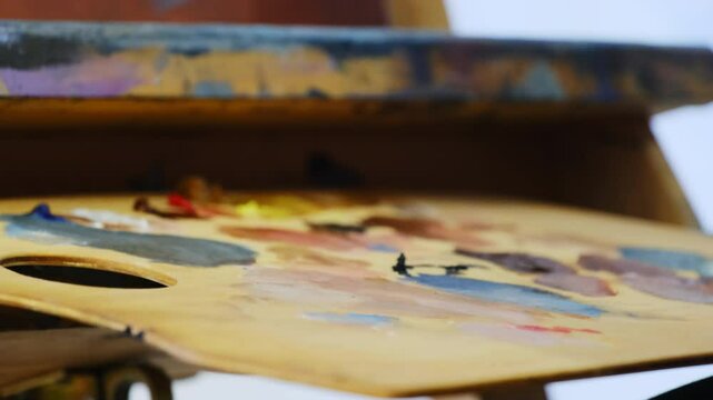 Artist uses large color palette and brush to form painting. Specialist works on sketch and creates special figure in art studio during lesson