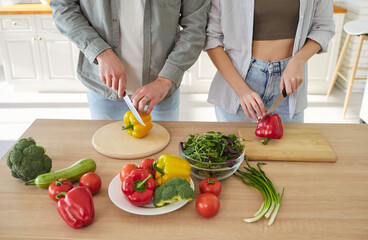Man and woman engage in food preparation, cutting colorful vegetables on wooden boards. Angled top view of hands of people cooking together at home, demonstrating teamwork in creating healthy meal.