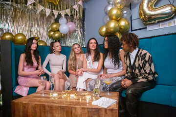 Group of female friends sitting on sofa with drinks during birthday party