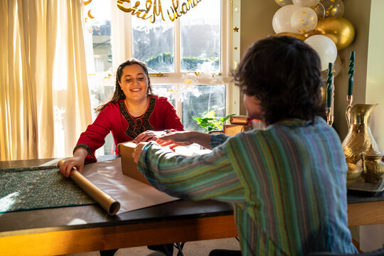 Adult siblings sitting at table and wrapping gifts for Eid Celebration
