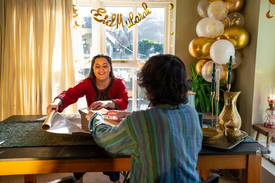 Adult siblings sitting at table and wrapping gifts for Eid Celebration