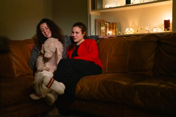 Obraz premium Lesbian couple sitting on sofa with dog at home on Valentines day
