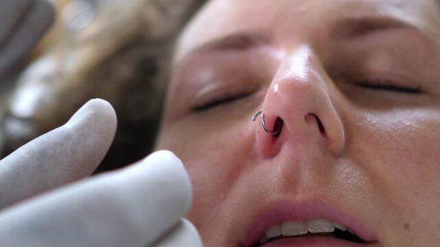 Professional piercer carefully inserting delicate nose ring using sterile catheter, ensuring precise placement and client comfort during precise body modification procedure