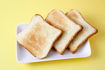 Three slices of bread in the shape of a square on a white flat plate surrounded by a yellow background. The three pieces, neatly arranged on a plate, reflect the concept of a morning lunch.