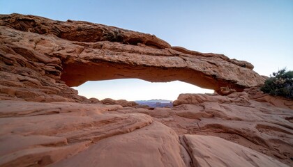 Desert arch frames distant landscape beneath a blue sky at sunset