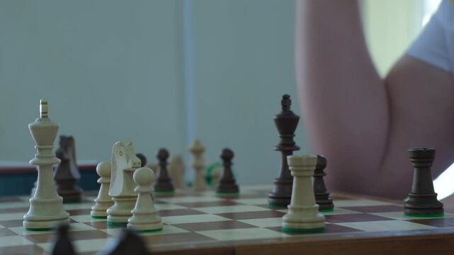 Man studies chessboard for long time before confidently moving king piece. Player moves piece and presses button on timer behind board