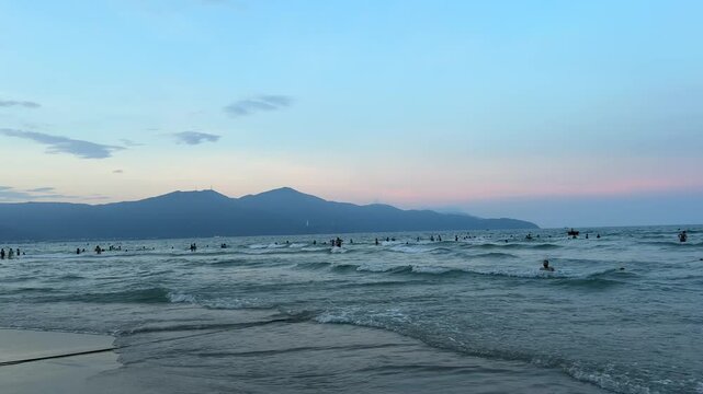 Sunset over sea waves washing the beach sand. Waves sunset mountains sun setting over mountain silhouette. Tropical natural sea view on Molang beach, Indonesia