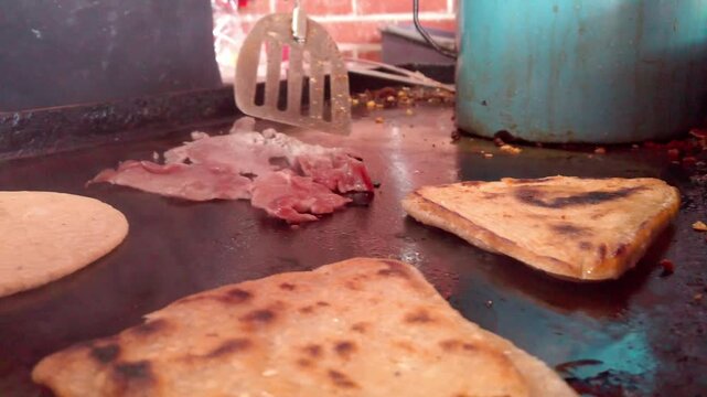 Close up slow motion of sliced meat, tortilla, and folded quesadillas grilling on hot flat-top with visible steam and spatula