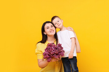 Mother and her son with bouquet of lilac flowers on yellow background
