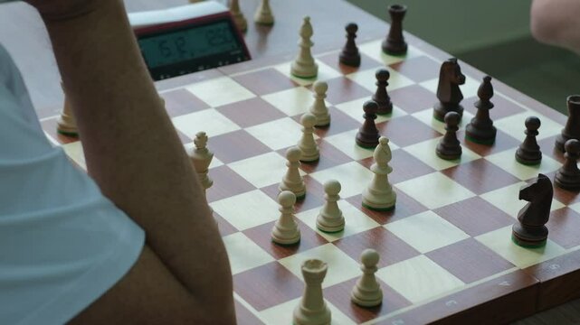 Chess players intensely think about moves while timer ticking. Men sit at table opposite each other and play chess in bright room
