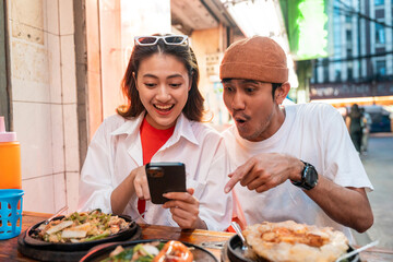 Asian couple man and woman enjoy eating street food noodle at night market. Traveler Asian couple blogger Happy tourists with Traditional food local road at thailand bangkok city.