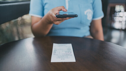 Woman scanning a receipt with a smartphone at a cafe, illustrating digital payment, expense...