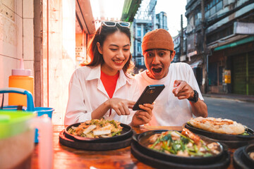 Asian couple man and woman enjoy eating street food noodle at night market. Traveler Asian couple blogger Happy tourists with Traditional food local road at thailand bangkok city.