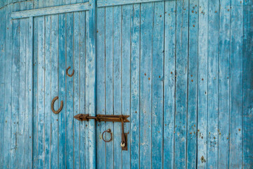 Portone di un fienile in legno , colorato di azzurro, con chiusura in ferro arrugginito e due ferri di cavallo arrugginiti

