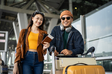 Happy asian couple walking through the airport terminal with luggage, using a smartphone at the...
