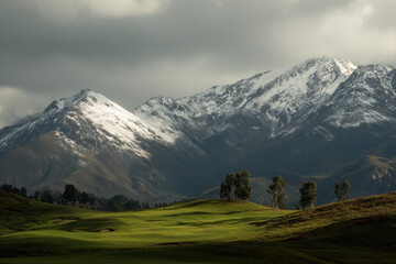 Fototapeta premium Lush green golf course with snowy mountain peaks under cloudy skies