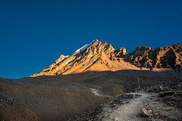 Trekking route to Thorung La pass against illuminated by rising sun Yakwakang peak. Annapurna circuit trek, Nepal.