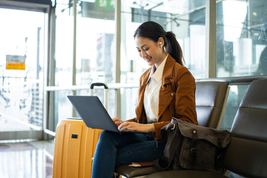 Confident young asian businesswoman working remotely online using laptop at the airport terminal while waiting for her flight, young female browsing the internet for emailing and managing e-business.