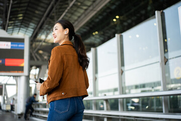 Portrait of confident young businesswoman smiling at camera ready traveling business trip with holding passport with ticket boarding pass and smartphone at the international airport terminal.