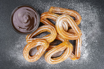 Traditional spanish dessert churros, fried dough pastry dusted with powdered sugar and chocolate sause on black background. Street food, sweet snack, homemade dessert. Top view, flat lay