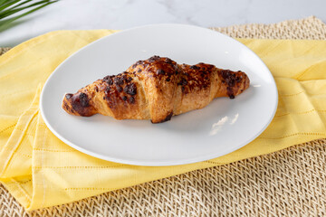 Delicious chocolate croissant resting on white plate with yellow napkin