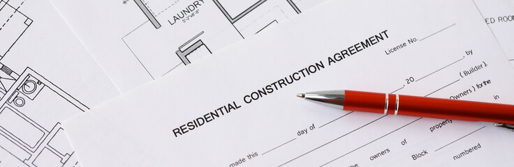 Pen on residential construction agreement and planning blueprints of residential building project...