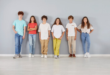 Obraz premium Group portrait of a diverse and positive team of a cheerful children, pupils and students stands together on a grey background. They are happy and united, showing friendship and teamwork.