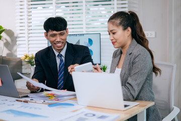 Fototapeta premium Cheerful Asian businessman and woman looking at laptop screen, analyzing project success in office.