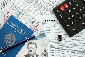 North Korean won money bills lies on table with pen, calculator, passport and tax forms