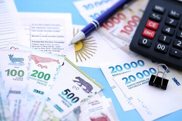 Argentine pesos money bills in big amount lies on table with pen, calculator, passport and tax forms