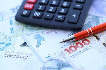 Argentine pesos money bills in big amount lies on table with pen and calculator close up
