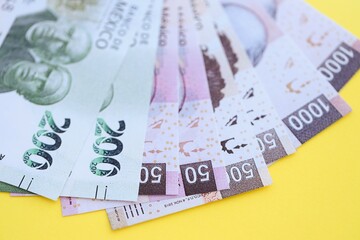 Mexican pesos money bills in big amount lies on yellow color table close up