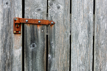 Close view of a rusty hinge attached to a weathered wooden door showcasing textures and natural wear evident in daylight.