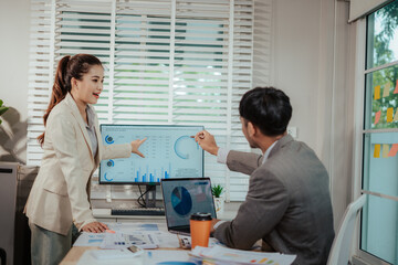 Fototapeta premium Cheerful Asian businessman and woman looking at laptop screen, analyzing project success in office.