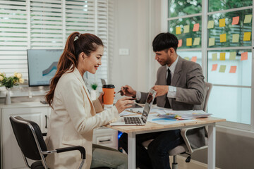 Fototapeta premium Cheerful Asian businessman and woman looking at laptop screen, analyzing project success in office.