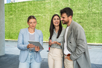 Diverse team of corporate professionals in formal attire collaborating outdoors, engaged in strategic discussion while analyzing data on laptop in front of modern glass office building.