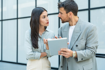 Obraz premium Diverse team of corporate professionals in formal attire collaborating outdoors, engaged in strategic discussion while analyzing data on laptop in front of modern glass office building.