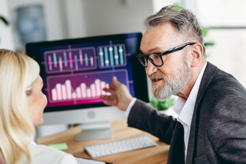 Senior professional discussing business strategies with a colleague in a modern office setting, showcasing teamwork