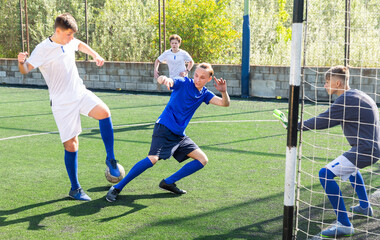 Junior football teams having golmouth scramble and struggling for ball