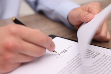 Man putting signature on document at table, closeup