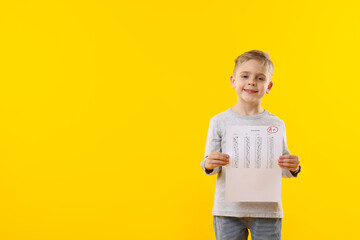 School grade. Little boy holding answer sheet with letter A and plus symbol on yellow background,...