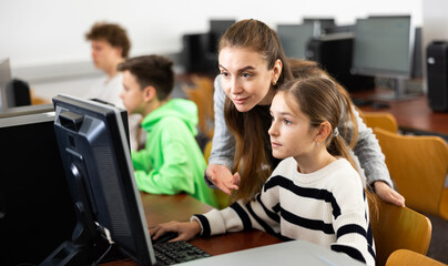 Fototapeta premium Friendly female teacher consulting interested focused teenage girl studying in information technology class..