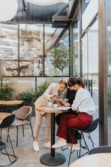 Fototapeta premium Three women discussing ideas over a tablet while working in a bright cafe.