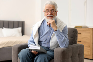 Fototapeta premium Handsome bearded man with book in armchair at home