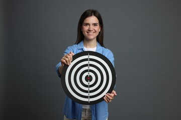 Targeting. Smiling woman with dart board on grey background