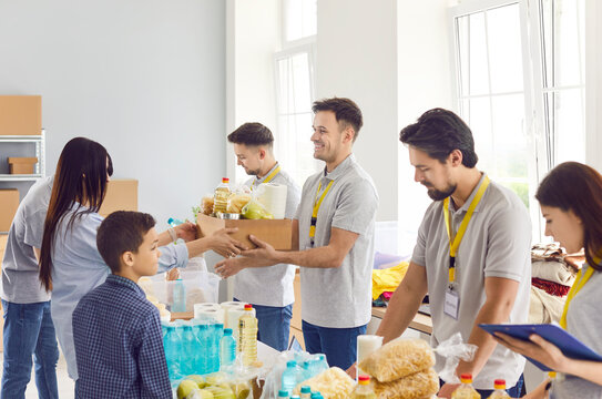 Helpful caring volunteer team giving free food and essentials donations in humanitarian aid to diverse refugees, making donation to people in need. Charity, food bank stocks, basic need provisions.