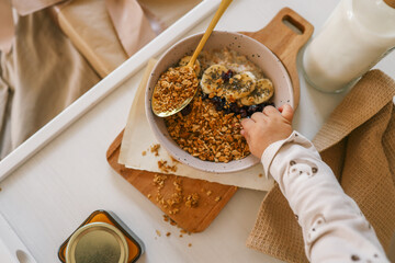 Close-up of child's hand reaching for granola in a breakfast bowl with banana, milk, and a gift box...