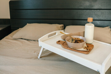 Flatlay of cozy breakfast tray with granola, milk, amber candle, and napkin on a soft beige bed. Warm tones and natural textures create a calm and peaceful morning scene